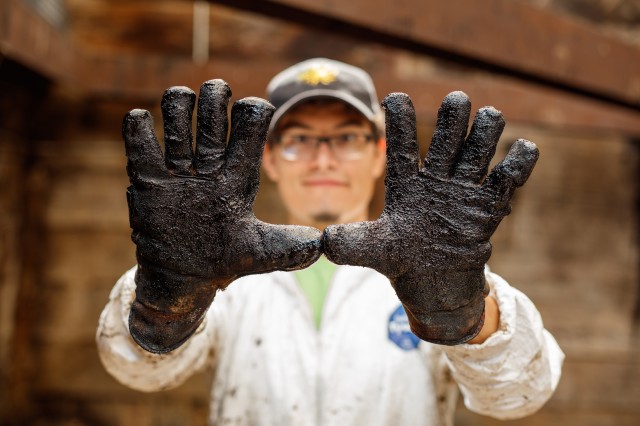 Photography of man with gloved hands entirely covered in "tar"