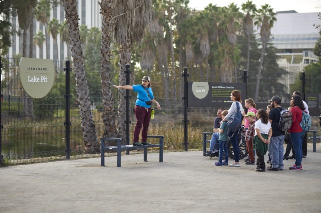 Museum Educator standing by a fence outside, speaking to a group of visitors