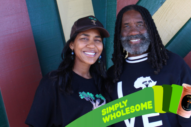 A wide, eye-level photograph shows two smiling people—a man and a woman—posed closely together inside Simply Wholesome, a restaurant and health food store in Los Angeles.