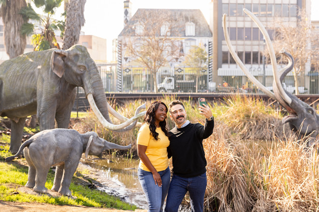 Couple holding up a camera to take a photo of themselves in front of mammoth sculptures