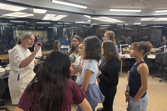 Students facing a scientist in a white lab coat holding up a fossil