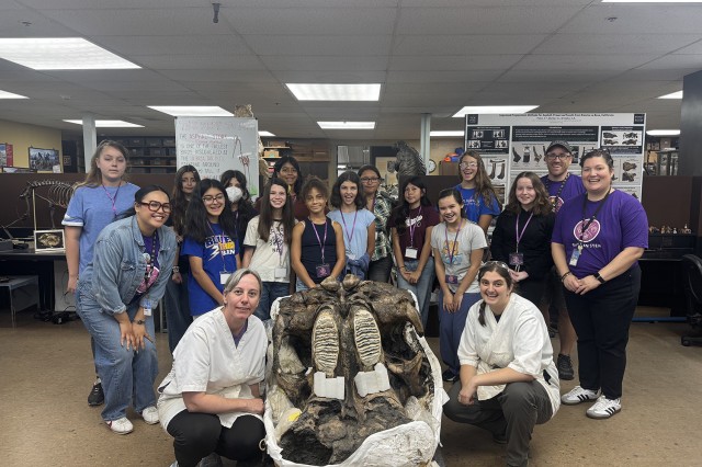 Students and scientists in white coats gathered around a fossil specimen