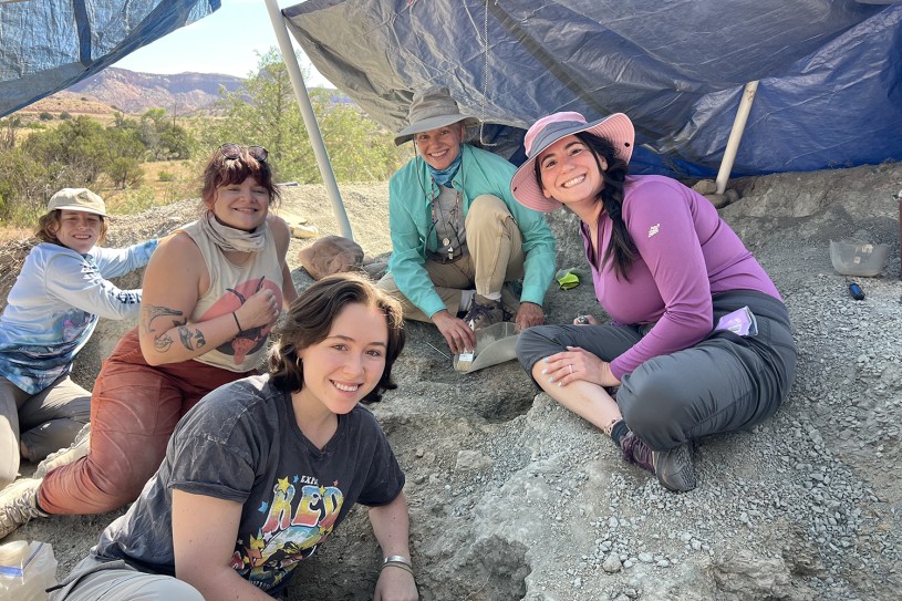 Bridget Altman and other volunteers sitting under a tent on a sandy, rocky ground