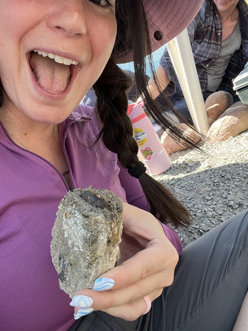Bridget Altman smiling wide and holding a specimen embedded in rock