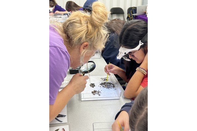 Collection Manager holding a magnifying lens over a tray of micro fossils that a student is sorting with a paintbrush