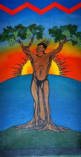 A vibrant painting of the Simply Wholesome logo: a brown-skinned figure with arms raised high, their body merging into a tree trunk with roots anchored in a green hill. The branches bear green leaves against a radiant orange and yellow sunset over blue water.