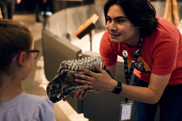 Intern holding a fossil specimen and leaning down towards a child visitor