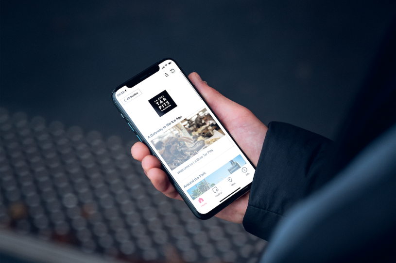 Hand Holding Phone showing Bloomberg Connects App for La Brea Tar Pits